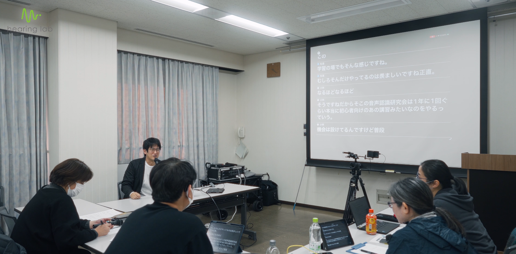 京都市聴覚言語障害センターで打ち合わせを行い、スクリーンと端末に字幕を表示している様子